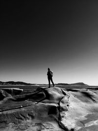 Rear view of woman standing on rock formation against clear sky