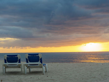 Chairs on beach against sky during sunset