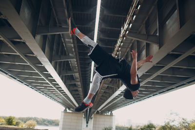 Low angle view of man jumping on bridge