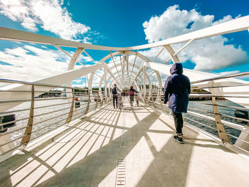 Rear view of men walking on footbridge against sky