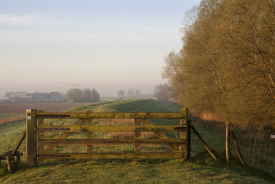 Wooden gate on field against sky during foggy weather