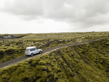 Aerial view of car driving through moss covered lava rocks in ic