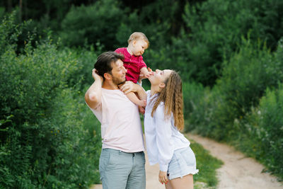 Happy young parents with a baby are walking through the forest