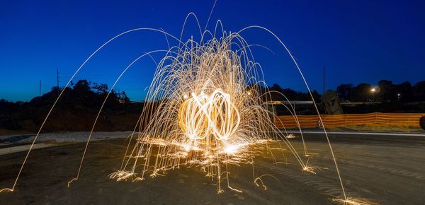 Firework display on beach against clear blue sky at night