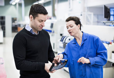 Mid adult female electrician explaining machine part to client in factory