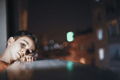 Portrait of boy leaning on window sill at night