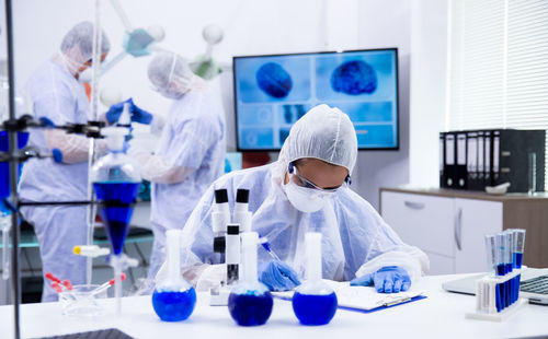 Doctor writing on file folder colleague in background at laboratory