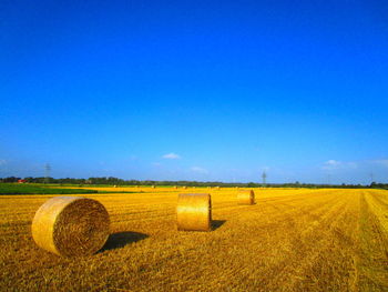 Hay bales on field against clear blue sky