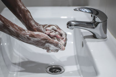 Close-up of hand holding faucet in bathroom