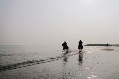 Silhouette people walking on beach against clear sky