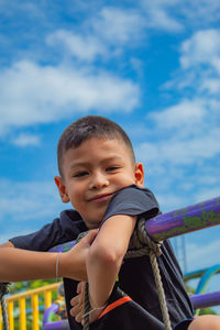 Portrait of cute boy by railing against sky