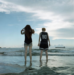 Rear view of friends standing at beach against sky