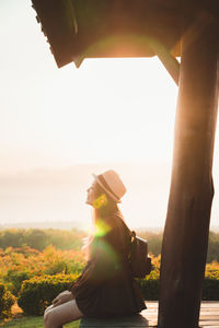 Side view of woman sitting against sky during sunset