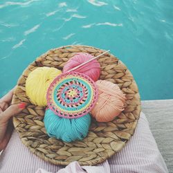 Midsection of woman holding wools in container while sitting at poolside