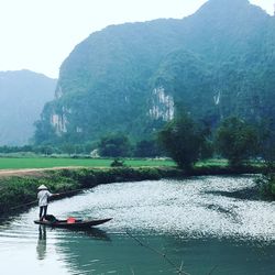 Rear view of man in boat on river against mountains