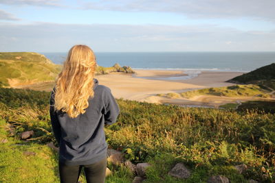 Rear view of woman standing by sea against sky