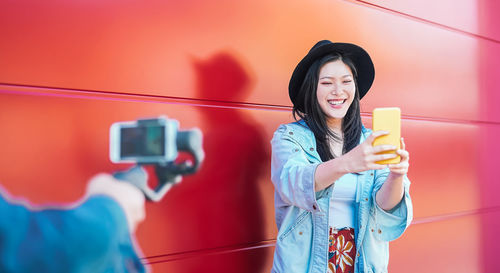 Cropped hand of person holding camera with woman taking selfie with mobile phone