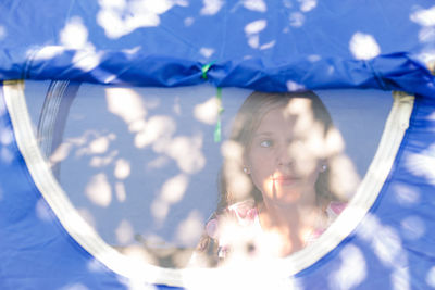 Girl sitting comfortably inside a camping blue tent behind a mesh anti-mosquito window, she 