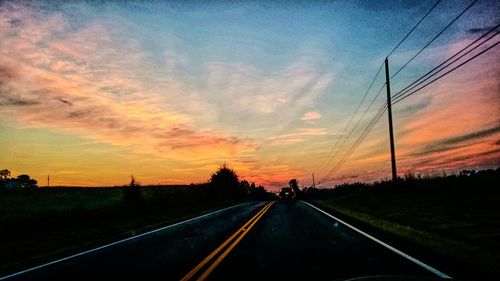 Road by silhouette trees against sky during sunset