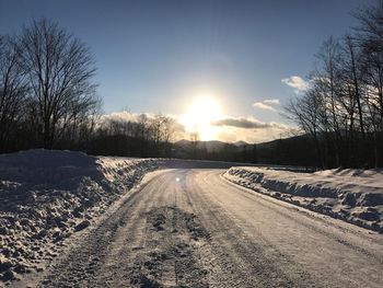 Snow covered road against sky during sunset