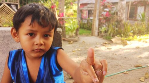 Portrait of boy showing obscene gesture against plants