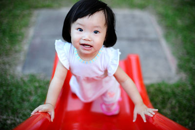 High angle view of cute girl playing on red slide at playground