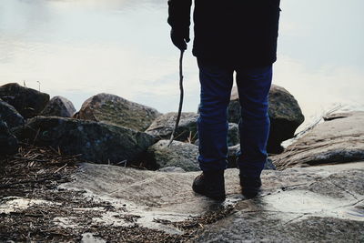 Low section of man standing on rock against sky