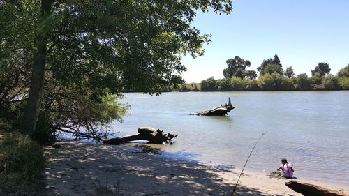 Man sitting on lake against clear sky