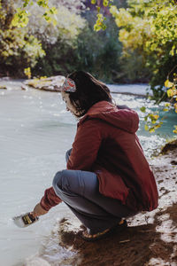 Woman taking water in container from flowing river in forest