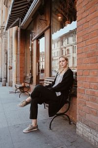 Portrait of woman sitting on bench against brick wall