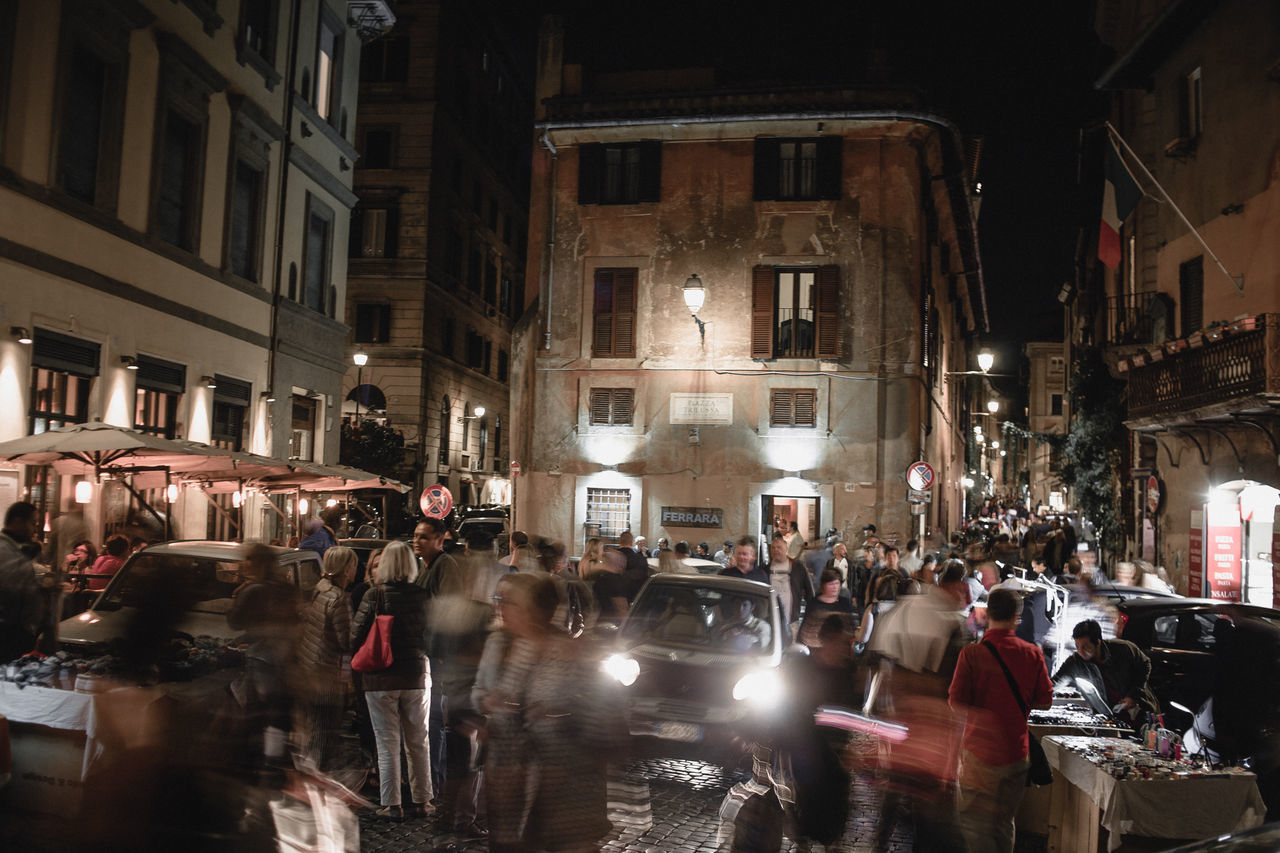 architecture, crowd, large group of people, building exterior, built structure, city, night, group of people, real people, illuminated, motion, street, blurred motion, transportation, women, men, mode of transportation, lifestyles, city life, outdoors, busy