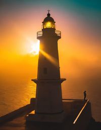 Lighthouse by sea against sky during sunset