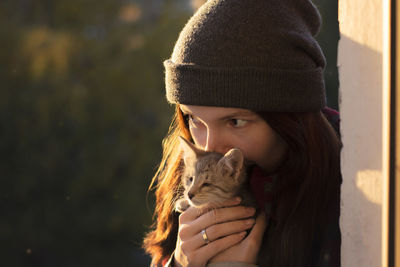 Close-up of woman kissing kitten by wall on sunny day