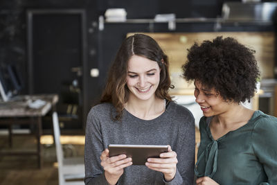 Two smiling young women sharing tablet in office