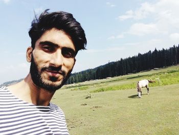 Portrait of young man with horse standing on field