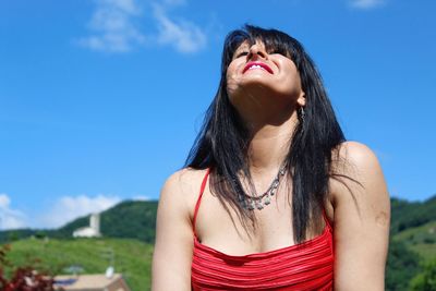 Low angle view of young woman with eyes closed standing against blue sky