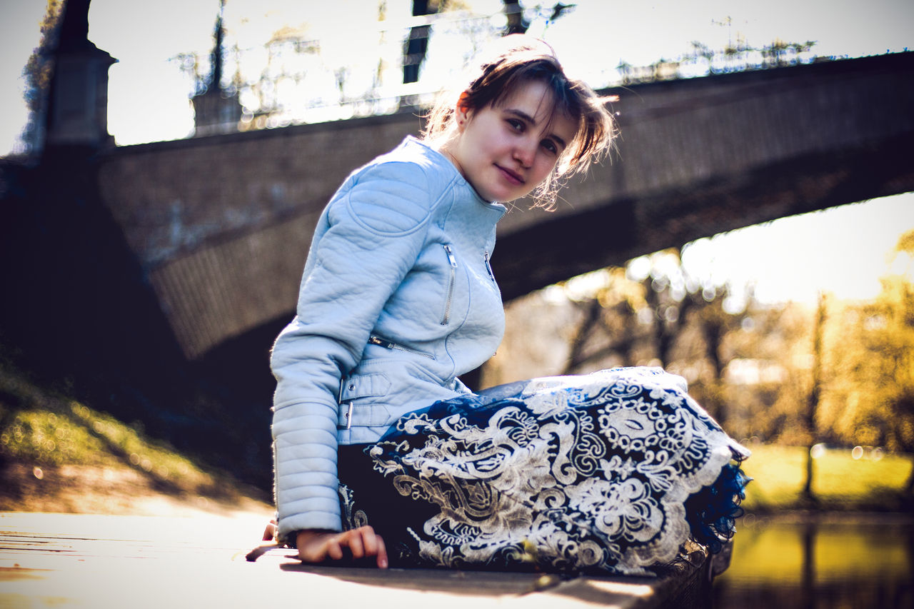 real people, one person, young adult, lifestyles, leisure activity, casual clothing, focus on foreground, young women, day, clothing, beauty, nature, architecture, looking, women, three quarter length, sitting, looking away, beautiful woman, outdoors, hairstyle