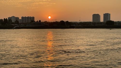 Scenic view of river by silhouette buildings against sky during sunset