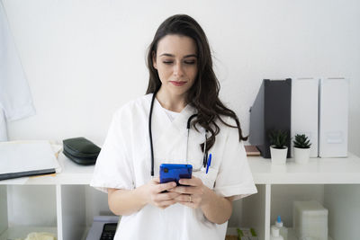 Female doctor text messaging on smart phone in clinic