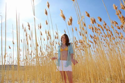 Low angle view of seductive girl standing in field against sky on sunny day