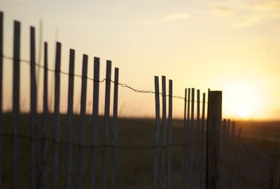 Fence on field against sky during sunset