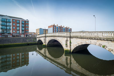 Bridge over river by buildings against sky