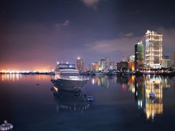 Boats in river by illuminated buildings against sky at night