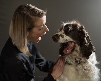 Close-up of woman and dog with mouth open against gray wall