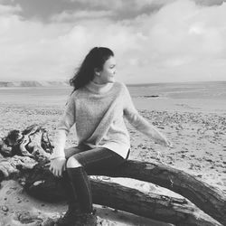 Young woman sitting on shore at beach against sky