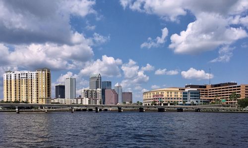 Buildings by river against cloudy sky