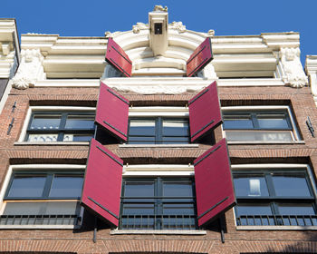 Low angle view of red shutters on a canal house in amsterdam against blue sky