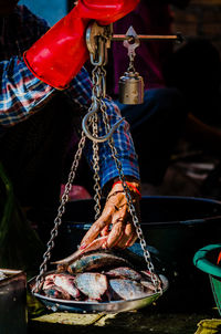 Cropped hands of market vendor weighing fish at stall