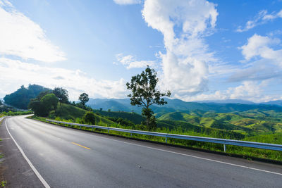 Road by trees against landscape and sky