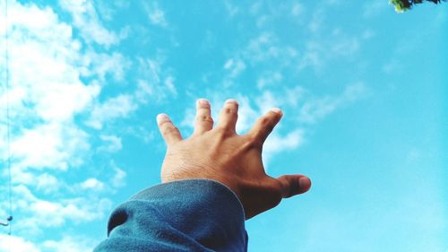 Low angle view of man hand against blue sky